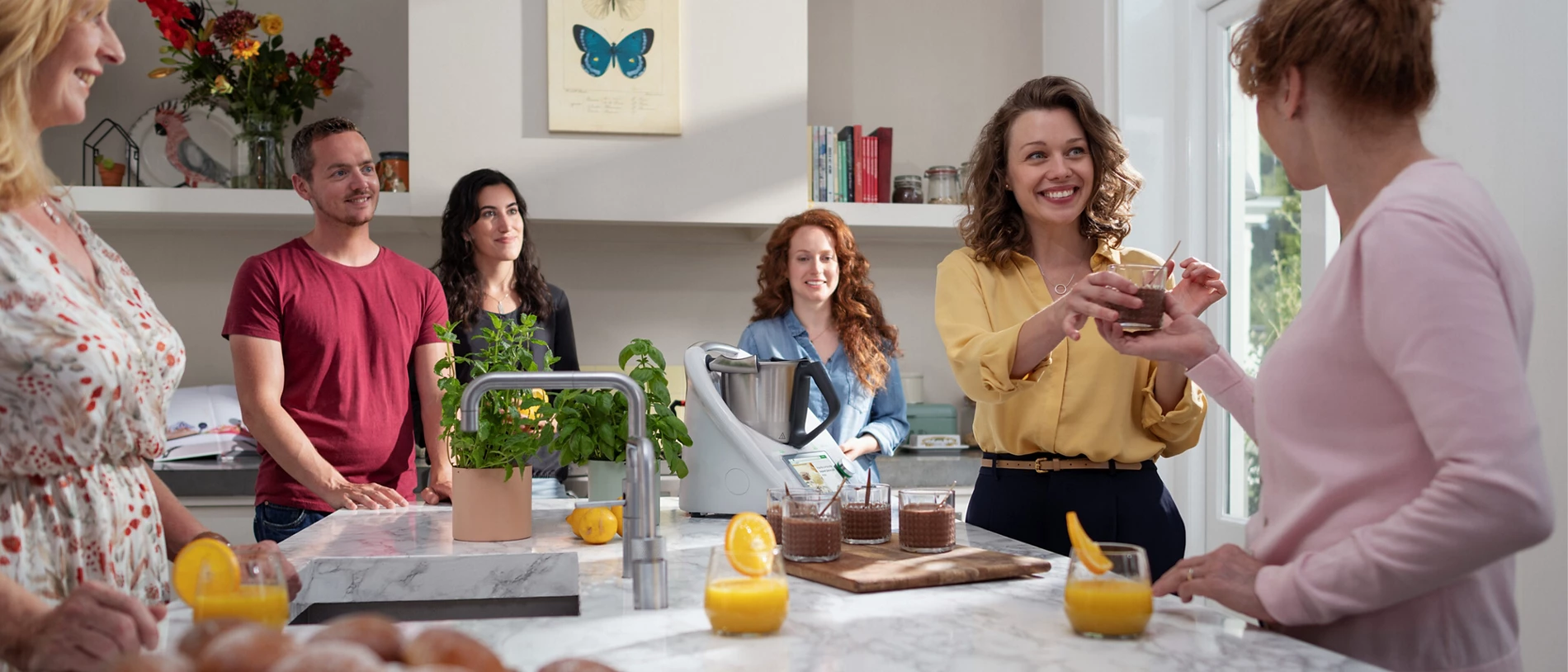 Smiling people in a bright kitchen enjoying a cooking demonstration.